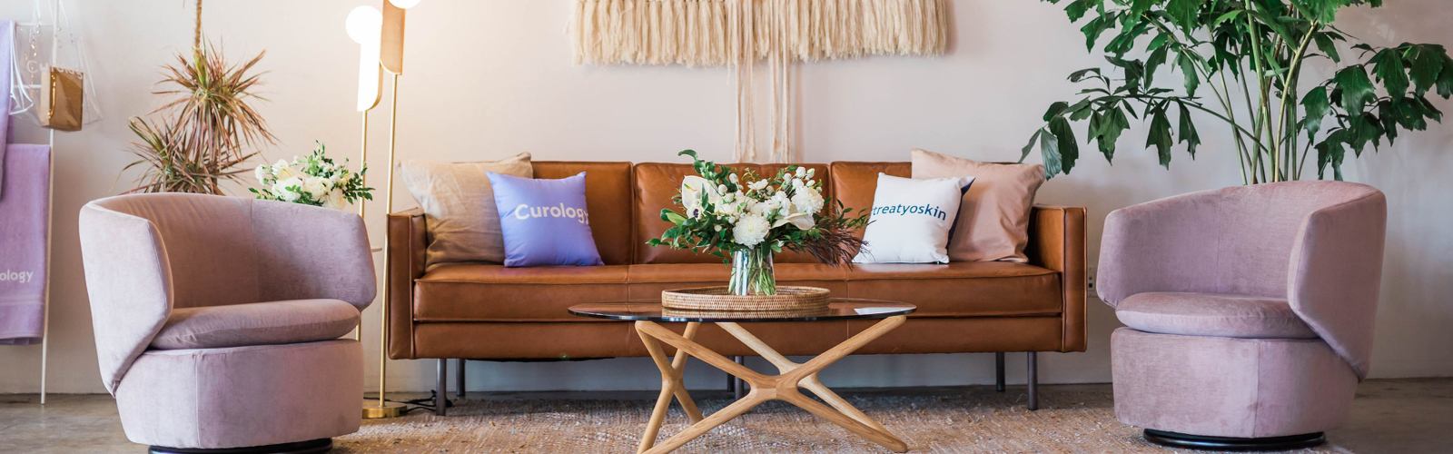 Brown leather couch with two pink chairs on either side and a coffee table infront.